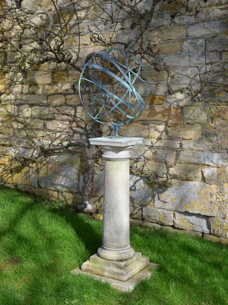 A verdigris patinated brass armillary sphere raised upon an carved Portland stone column pillar pedestal 